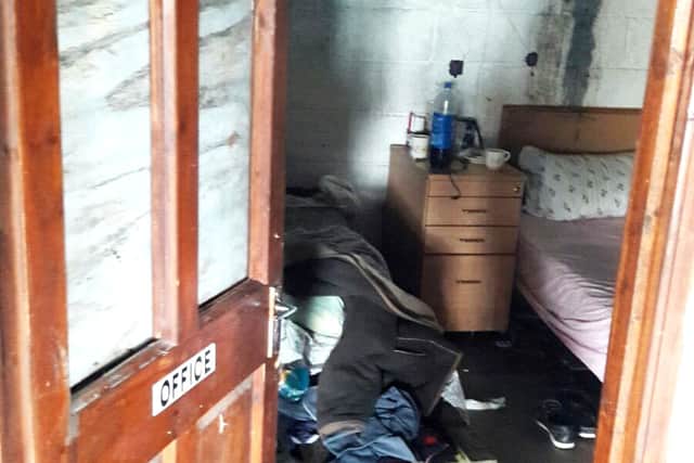 Inside a damp shed-like building, several mattresses are propped up on wooden crates as mildew can be seen on the walls.