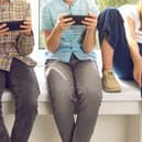 Children sitting on windowsill immersed in their mobile phones