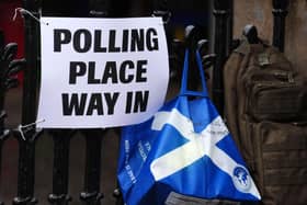 A polling place sign on a fence, with a bag featuring the Scottish saltire hanging beside it