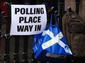A polling place sign on a fence, with a bag featuring the Scottish saltire hanging beside it
