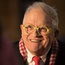 Headshot of David Hockney smiling, wearing yellow-rimmed round glasses