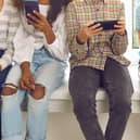 Children sitting on windowsill immersed in their mobile phones