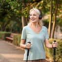 Mature happy woman walking in a park with walking poles while wearing headphones