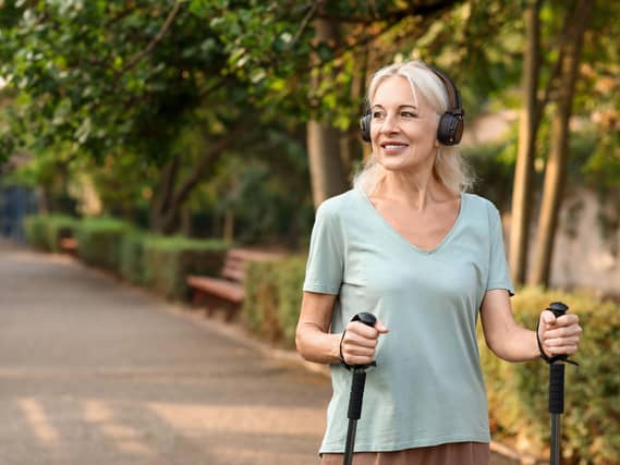 Mature happy woman walking in a park with walking poles while wearing headphones