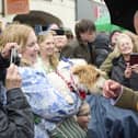 The King's hand is sniffed by a dog being held up by a woman in a crowd of well-wishers