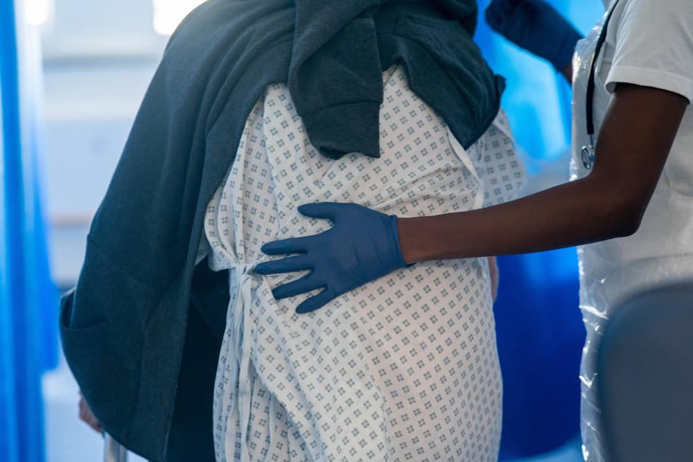 A hospital patient being assisted with walking through a ward by a member of staff