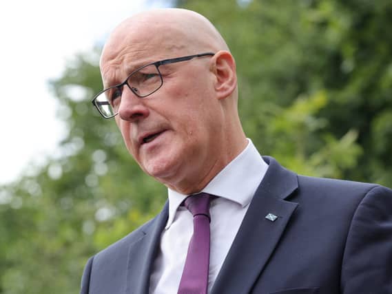 Headshot of John Swinney speaking outside, with trees behind him