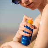 Young woman in sunglasses holding bottle of sunscreen