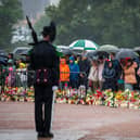 Mourners under umbrellas, with floral tributes on the ground in front of them