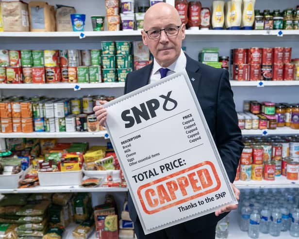 John Swinney in a shop, holding up a sign advertising the SNP's food price cap proposal