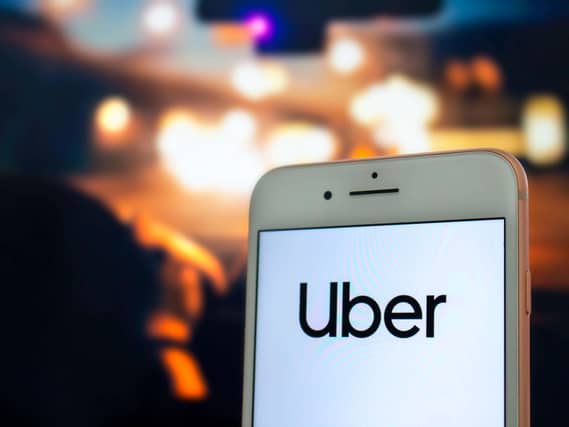 An iPhone with the Uber app open being held by a passenger in the back seat of a car