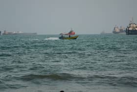 A swimmer remains near the shore as a motorboat passes commercial vessels anchored in the Strait of Hormuz
