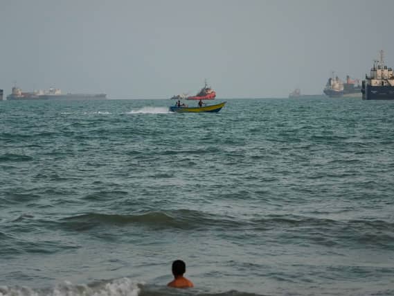 A swimmer remains near the shore as a motorboat passes commercial vessels anchored in the Strait of Hormuz
