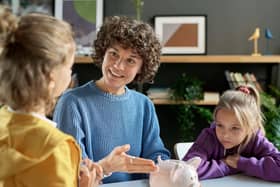A mother pointing at a piggy bank and teaching her children to save money while they sit at table