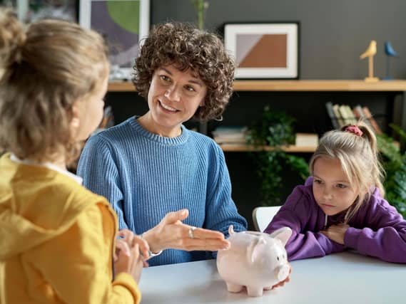 A mother pointing at a piggy bank and teaching her children to save money while they sit at table