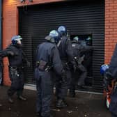 Police officers in protective helmets enter a property through a shutter
