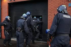 Police officers in protective helmets enter a property through a shutter
