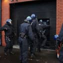 Police officers in protective helmets enter a property through a shutter