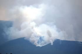 A view of a wildfire on a hillside, with smoke rising from it