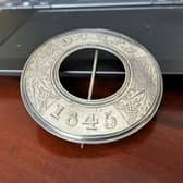 View of a silver brooch, which has the middle cut out, with an inscription round the edge