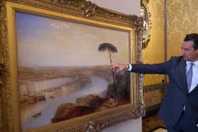 A man in a suit pointing at a landscape picture of Rome