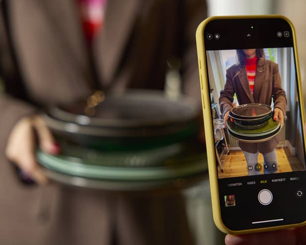 A mobile phone in the foreground taking a picture of some crockery being held by a woman