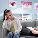 A child on a sofa while a woman seated nearby writes on a clipboard