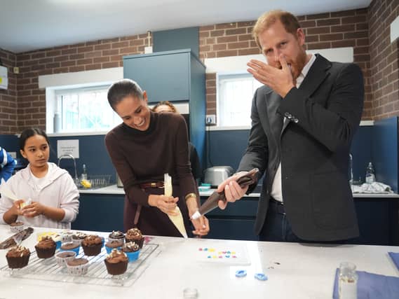 Harry licks icing from his hand as he and the Meghan decorate birthday cupcakes during a visit to Epic Partners in Nottingham
