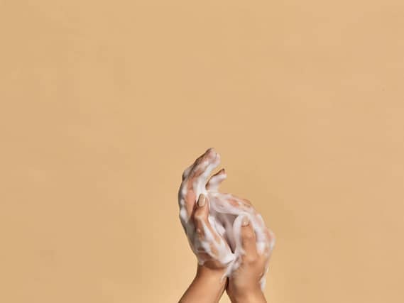 Two hands with hand soap foam on colorful background with copy space.