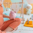 Cropped image of pregnant woman, who is wearing orange dungarees, sitting in a nursery room holding a piggy bank