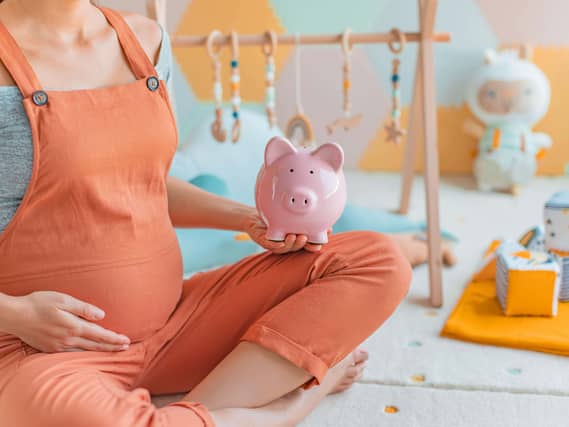 Cropped image of pregnant woman, who is wearing orange dungarees, sitting in a nursery room holding a piggy bank