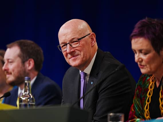 John Swinney sitting on a desk on stage