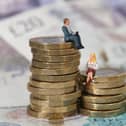Models of a man and woman stand on a pile of coins and bank notes