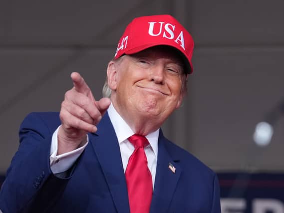 Donald Trump in a red baseball cap points towards a crowd at a rally