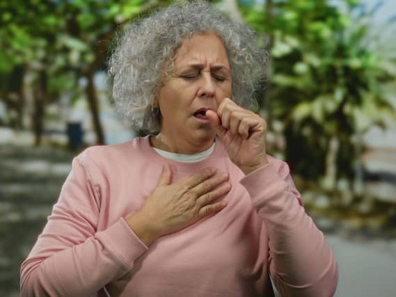 Senior woman coughing into her fist and placing her other hand on her chest in a park
