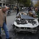 A man walks past a burned-out car in Paris after a quiet Monday night under curfew