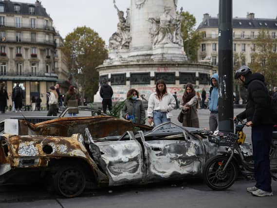 People examine a burned-out car after a quiet night on Monday under curfew in Paris