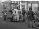 Troops on patrol in the Falls Road area of Belfast encounter a civilian by an overturned car that formed a barricade during rioting in 1981