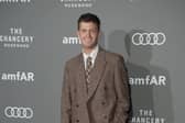 Jamie Miller smiling while posing for photos at a red carpet event, wearing a brown suit