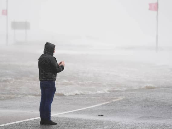 A man looks at a flooded road amid blustery weather