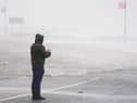A man looks at a flooded road amid blustery weather
