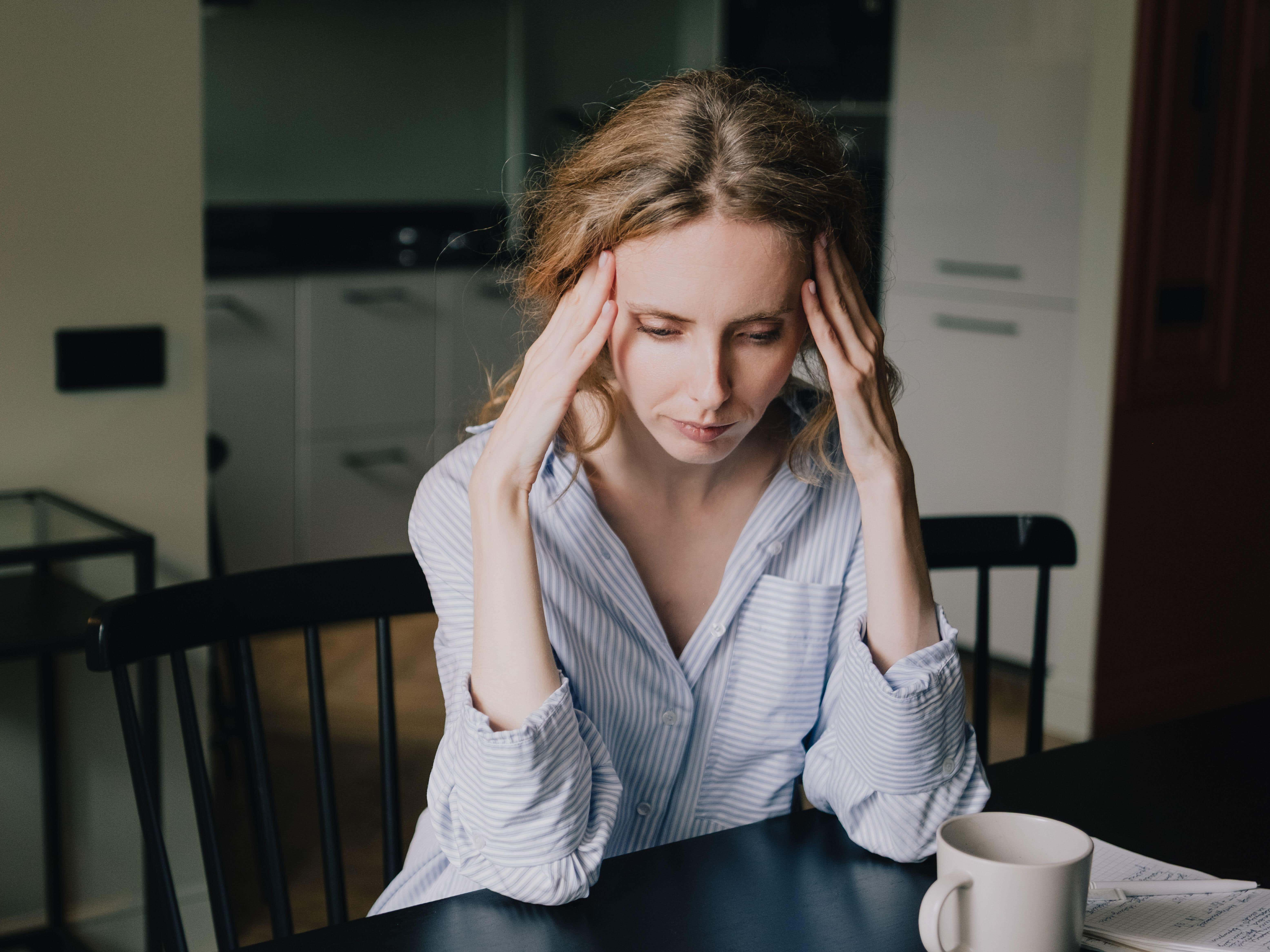 Stressed pale woman pressing both hands against her temples while sitting at a table at home