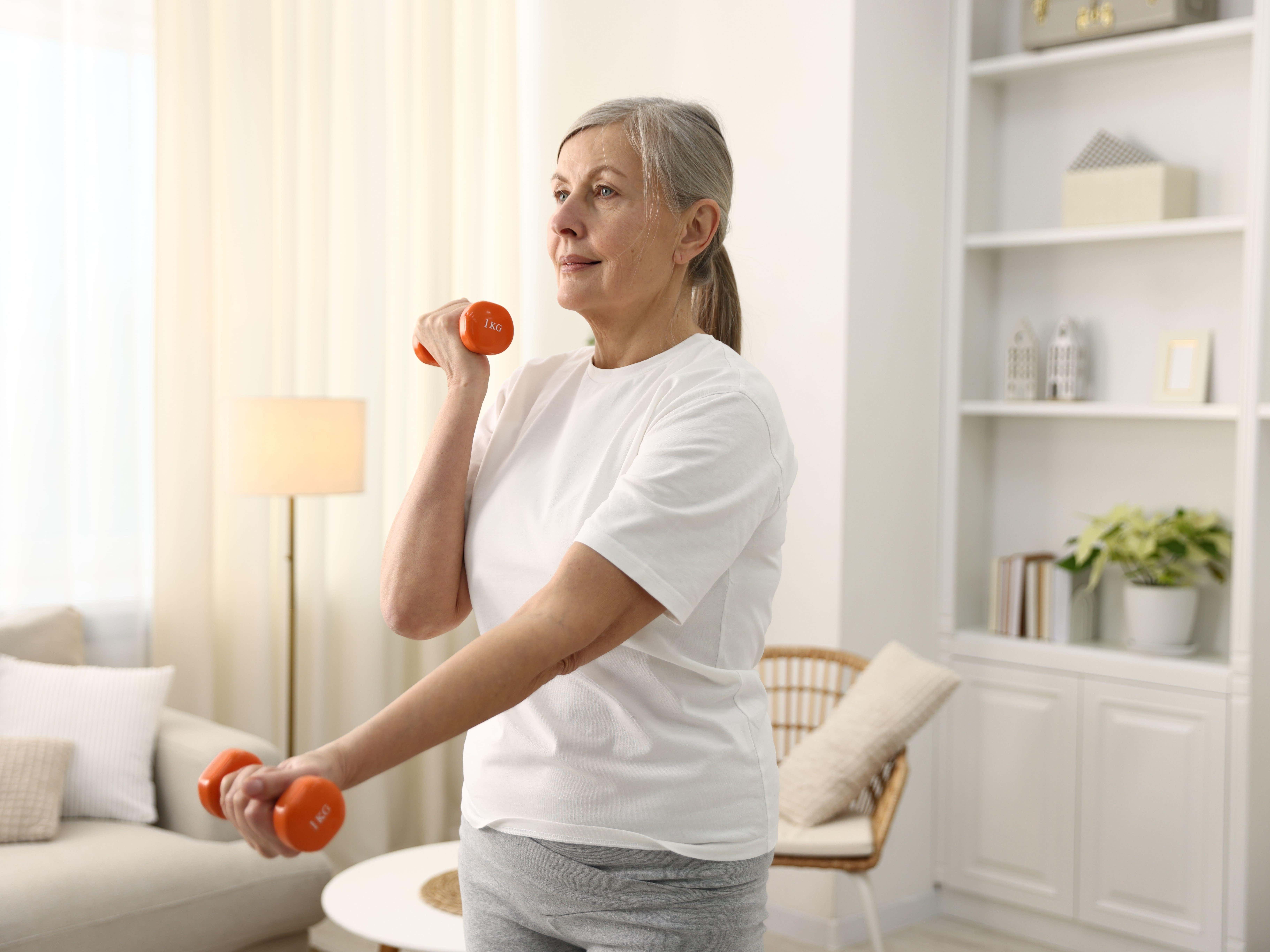 Senior woman exercising with dumbbells at home.