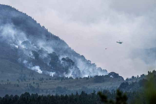 A helicopter carrying water tackles the wildfire burning near Nethy Bridge in the Cairngorms National Park in July (PA)