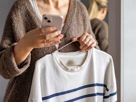 woman holds smartphone while inspecting clothing item preparing listing for online resale