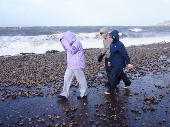 People with their coat hoods up walk on a beach