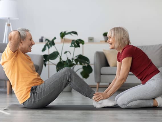 Happy senior couple doing sit ups at home on yoga mat