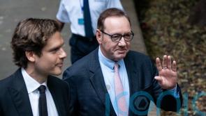 Kevin Spacey smiles and waves as he arrives at court for sex offences trial