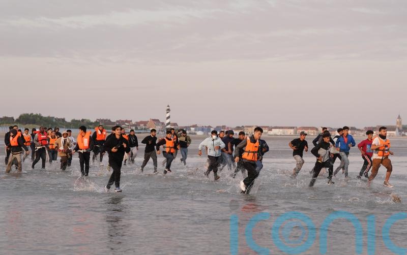 Migrants run across beach to board dinghy in the Channel