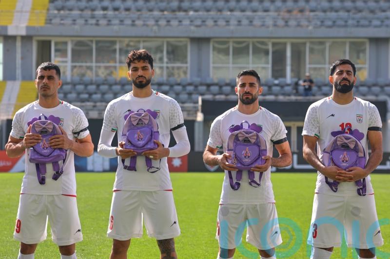Iran wear black armbands and hold schoolbags during national anthem before match